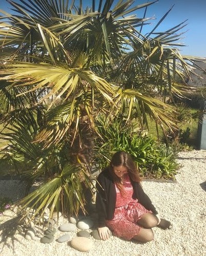 Miss Mulsant is ....... the palm tree. (palmier)