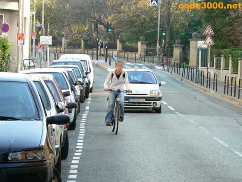 Cette cycliste circule trop près des véhicules en stationnement :